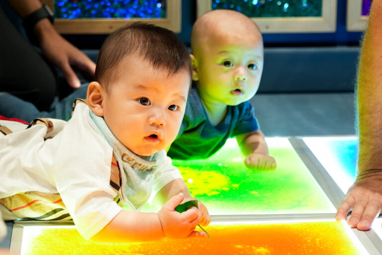 A baby and toddler exploring colors and textures on a light table at Acorn Playhouse, Southside Hong Kong.